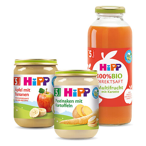 Drei Gläschen Babynahrung, jedes mit einer anderen Frucht und einem Prozentsatz an biologischem Inhalt beschriftet, begleitet von einer Flasche 100% biologischen Fruchtsafts.