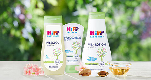 Eine Reihe von Babypflegeprodukten von Hipp, darunter eine Körperbutter, ein Massageöl und eine Körperlotion, die alle mit natürlichen Inhaltsstoffen gekennzeichnet sind und vor einer grünen Kulisse präsentiert werden.