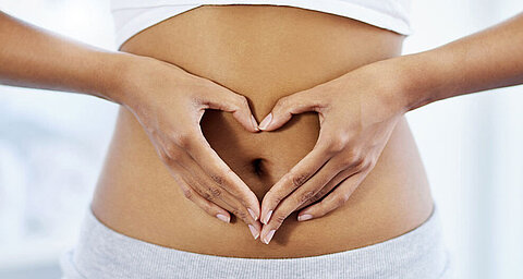 Eine Person formt eine Herzform mit ihren Händen über dem Bauch.