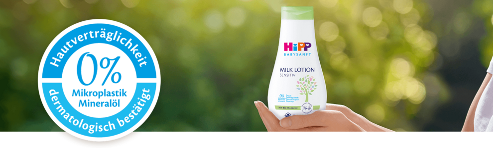 Eine Flasche eines Babypflegeprodukts mit der Aufschrift "Hipp Baby Sensitive" und einem Etikett mit der Aufschrift "0% Mikroplastik Mineralol" sowie eine Hand, die das Produkt vor einem grünen Hintergrund hält.