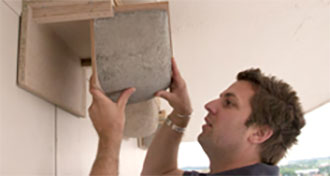 Ein Mann untersucht eine Holzkonstruktion, die an einer Wand befestigt ist, und hält einen gräulichen Gegenstand.